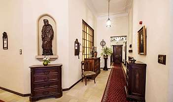 Couloir avec meubles en bois sombre, statue, tapis rouge et lustre au plafond