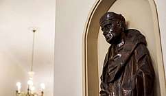 Statue en bois foncé d'un homme avec chapeau et manteau dans une niche