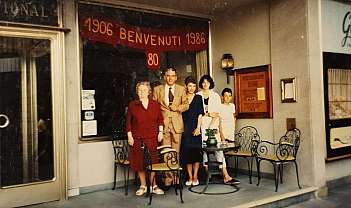 Cinq personnes debout devant un établissement avec des tables et des chaises en fer forgé