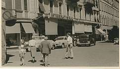 Personnes marchant sur une rue devant un bâtiment avec une enseigne International et des voitures anciennes garées