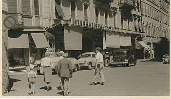Personnes marchant sur une rue devant un bâtiment avec une enseigne International et des voitures anciennes garées