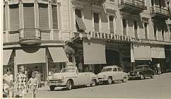 Voitures anciennes garées devant un bâtiment avec des personnes marchant dans la rue