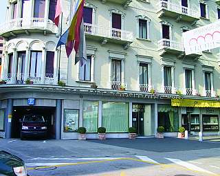 Façade d'un hôtel avec balcons, drapeaux et une voiture garée à l'entrée