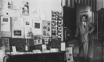 Homme en costume formel dans un bureau avec un mur couvert de prospectus et une table avec des documents
