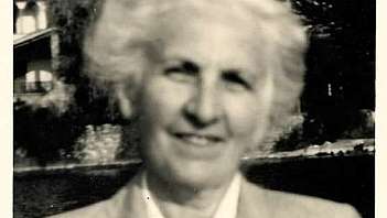 Donna anziana sorridente con capelli bianchi e giacca chiara all'aperto