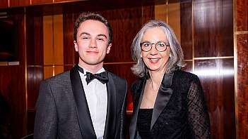 Giovane uomo e donna matura sorridenti in abiti da sera neri in ambiente interno