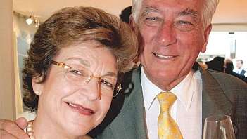 Coppia anziana sorridente in abiti eleganti, uomo con bicchiere di vino bianco