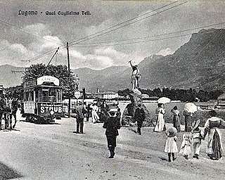 Vue historique du bord du lac de Lugano avec des personnes, une calèche, un tramway et la statue de Guillaume Tell