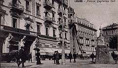Vue historique en noir et blanc de la Piazza Guglielmo Tell à Lugano avec des statues et des personnes en costumes d'époque