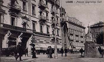 Vue historique en noir et blanc de la Piazza Guglielmo Tell à Lugano avec des statues et des personnes en costumes d'époque