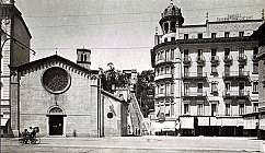 Place avec une église historique à gauche et un hôtel avec balcons à droite, escalier au centre