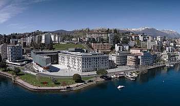 Vue panoramique d'une promenade au bord du lac avec des bâtiments, un parc et des montagnes en arrière-plan