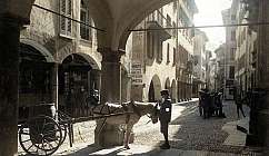Kopfsteinpflasterstraße mit Bögen, Mann in historischer Kleidung und Pferd mit Wagen