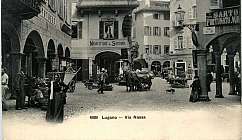 Vue historique de la Via Nassa à Lugano avec des personnes, un chariot tiré par des chevaux et des bâtiments avec des portiques