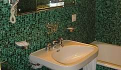 Évier blanc avec miroir et sèche-cheveux sur un mur carrelé vert