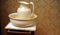 Cruche blanche avec bord doré dans une bassine blanche sur une table de chevet en bois