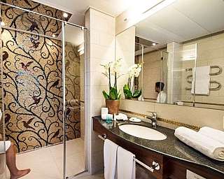 Salle de bain avec lavabo, grand miroir, mur avec mosaïque décorative et femme en peignoir assise