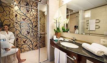 Salle de bain moderne avec lavabo, grand miroir, mur en mosaïque et femme en peignoir assise