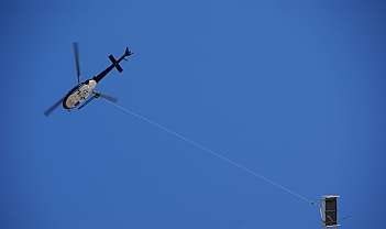 Hélicoptère noir et blanc transportant une charge suspendue par une corde dans le ciel bleu