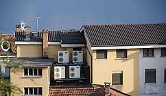 Quatre unités extérieures de climatiseurs montées sur un bâtiment avec un toit en tuiles