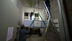 Trois ouvriers installent un grand dispositif suspendu dans une pièce aux murs en béton