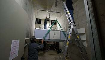 Trois ouvriers installent un grand dispositif suspendu dans une pièce aux murs en béton