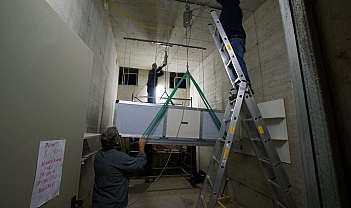 Trois ouvriers installent un grand équipement suspendu dans une pièce aux murs en béton