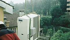 Technicien avec casque installe une unité extérieure de climatisation suspendue sur le toit