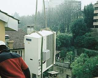 Technicien avec casque installe une unité extérieure de climatisation suspendue sur le toit