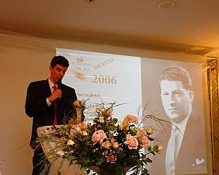 Homme en costume parlant au micro avec projection d'une photo historique et des fleurs au premier plan