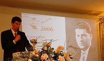 Homme en costume parlant au microphone avec projection d'une photo historique et fleurs au premier plan