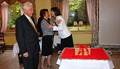 Deux femmes se saluent en s'embrassant tandis qu'un homme sourit dans une pièce avec des rideaux floraux