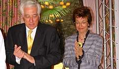 Deux personnes en tenue formelle devant une table avec un paquet cadeau orné d'un nœud rouge