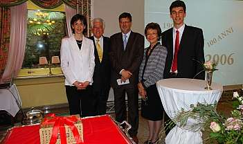 Cinq personnes en tenue formelle lors d'un événement avec des décorations et une table avec un nœud rouge