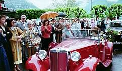Voiture ancienne rouge avec des personnes autour lors d'un événement en plein air