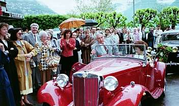 Voiture ancienne rouge avec des personnes autour lors d'un événement en plein air
