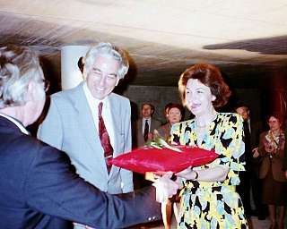 Femme en robe fleurie recevant un paquet rouge d'un homme en veste lors d'un événement formel