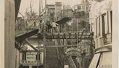 Ouvriers travaillant sur une structure en bois devant un escalier et un funiculaire dans une ville historique