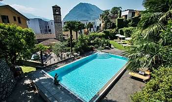 Piscine rectangulaire dans un jardin avec des palmiers, des chaises longues et une montagne en arrière-plan