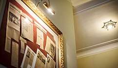 Cadre doré avec des articles de journaux exposés sur fond rouge éclairés par une lampe