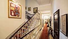 Couloir intérieur avec escalier en marbre et rampe décorée, tapis rouge et tableaux aux murs