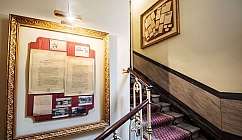 Escalier avec rampe en fer forgé et cadres avec documents historiques encadrés