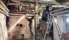 Deux ouvriers travaillant sur des tuyauteries dans un environnement industriel avec des étincelles