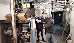 Quatre hommes discutent de documents dans une cave avec des tuyaux et des équipements techniques