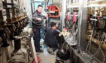 Deux techniciens installent et connectent des câbles dans une salle technique avec des conduits et des tableaux électriques