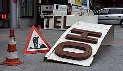 Panneaux de travaux en cours et cônes de signalisation sur un trottoir urbain avec des véhicules stationnés