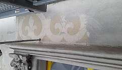 Détail de décoration murale avec motifs floraux fanés au-dessus d'un cadre en pierre