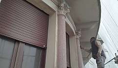 Homme travaillant sur des colonnes d'un bâtiment avec des volets fermés