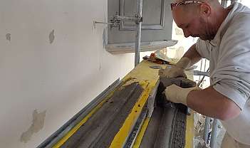 Maçon avec des gants applique du mortier sur une surface en bois jaune