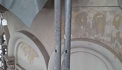 Mur avec des fresques anciennes partiellement détériorées et des tuyaux métalliques au premier plan